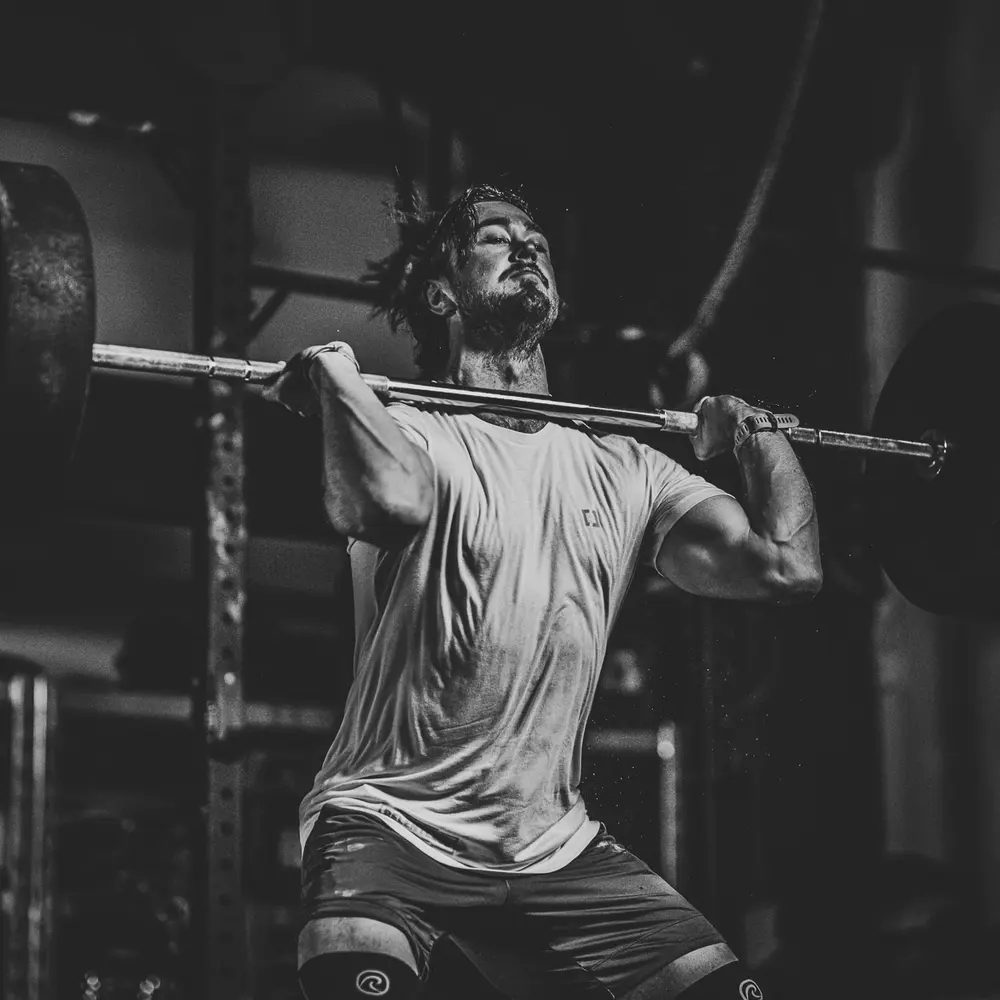 An athlete finishing a barbell lift overhead in a CrossFit box.